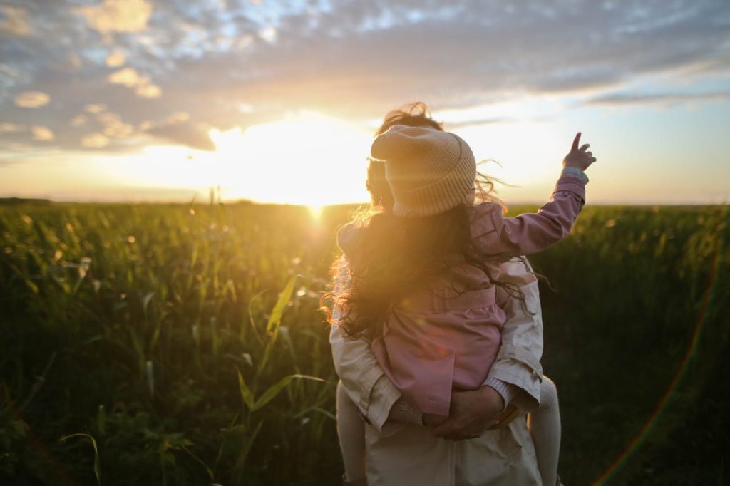 mother-and-daughter-on-grass-1683975 A mother and daughter embrace and point at the sunset in a grassy field.